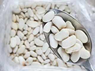 White beans in a spoon, a pile of beans in the background. Legumes. Groceries. Bean dishes. 