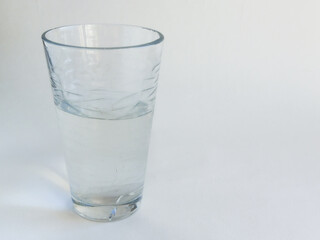 A transparent glass glass of water stands on the table, on a white background. Maintaining the body's water balance. Clean filtered water.