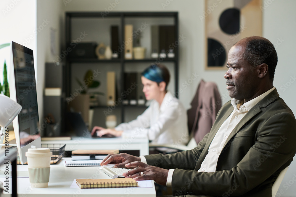 Poster side view of elegant mature male office manager looking at screen of desktop computer while analyzin