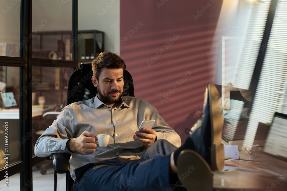 Aufkleber smiling male manager with cup of coffee texting in smartphone while sitting in armchair and keeping 