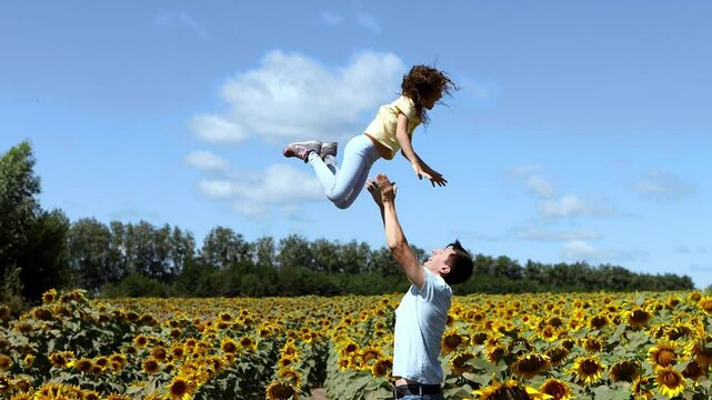 Dad throws up his little daughter. Father and daughter of European appearance walking in a field of sunflowers in slow motion. Field of sunflowers in summer. 4k footage