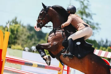 Rolgordijnen zonder boren Rider jump to clear the obstacle on the dark tail bay horse. Equestrian Sports, Show Jumping. Bay horse on course © Iuliia