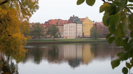 Fototapeta premium A Row of Buildings Reflected in a Calm River with Autumn Foliage Framing the View