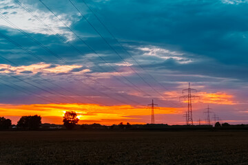 Fototapeta premium Summer sunset with a dramatic sky and overland high voltage lines near Tabertshausen, Deggendorf, Bavaria, Germany