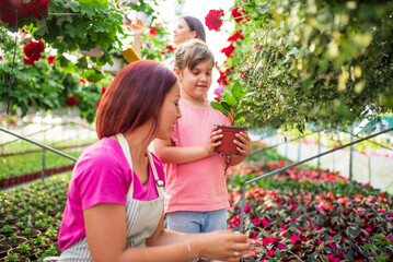 Gardener woman and little girl choosing blooming plant in greenhouse