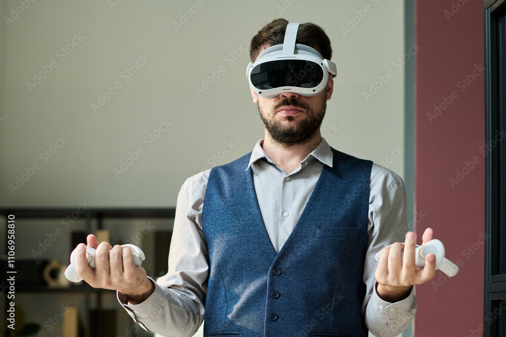 Poster Young businessman with remote controllers of virtual reality headset standing in front of camera while preparing presentation