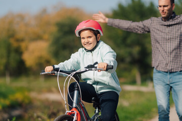 Obraz premium Father teaches daughter riding bike wearing helmet in a park