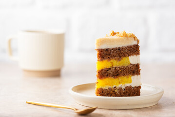Piece of pumpkin or carrot layered cake with coconut cream and orange confit with cup of coffee on a light background. Sugar, gluten and lactose free. Vegan, healthy dessert.