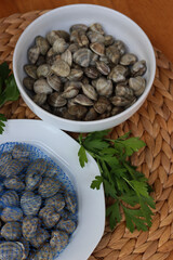 Many littleneck fresh clams in a white bowl with parsley leaves on wooden table