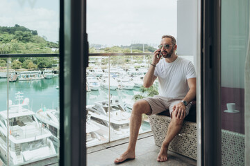 Man in a white T-shirt talking on the phone on a balcony 