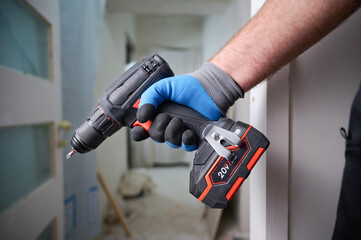 Construction worker holding electric cordless screwdriver in hand at construction site. Accessories...