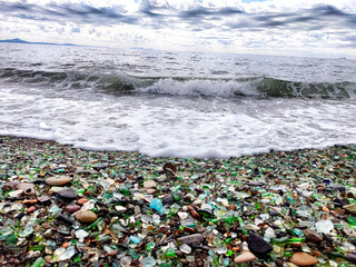 A beach with pebbles, glass and an incoming wave. Glass Bay in Vladivostok. Partial focus