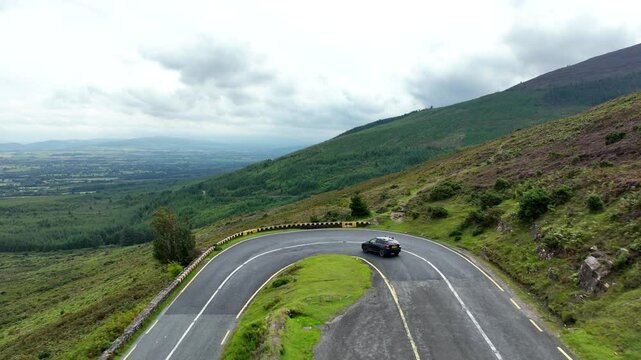 A black car enters a sharp turn on a mountain road
