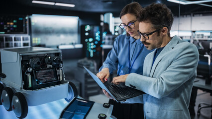 Portrait of Male and Female Engineers Developing a Remotely Controlled Robot in an Industrial...