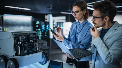 Portrait of Two Colleagues Working in a Research Facility, Using Laptop Computer to Develop a Futuristic Robot for Autonomous Deliveries. Engineers Working on Improving Detectors on their Prototype 