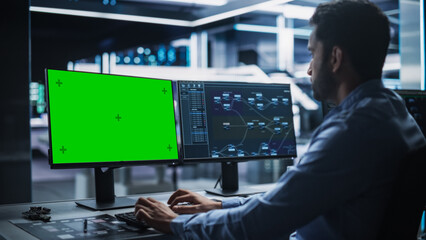 Professional Male IT Technical Support Specialist and Software Developer Working on Computer with Green Screen Mock-display in Monitoring Control Room. Programmer Fixing Hiccups in Service