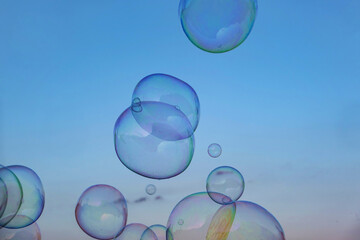 Magical soap bubbles floating in light blue sky with rainbow reflections