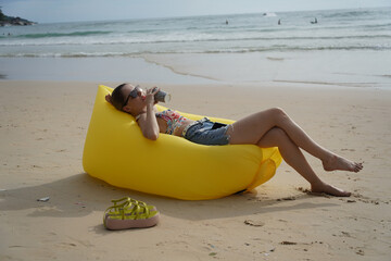 A young woman on the beach lounging on a yellow bean bag 