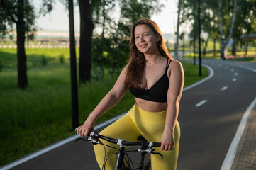 Naklejka premium A Caucasian woman in yellow leggings and a crop top rides a bicycle in tights in the park.