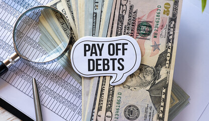 On a white surface are dollars on which a pen and paper with the inscription - Pay off Debts