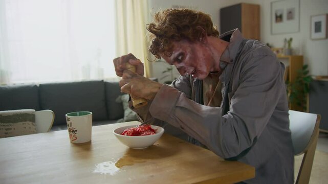 Medium side shot of grinning male zombie having breakfast before going to work, spicing bowl of raw meat with pepper grinder, taking spoonful with shaky hands then dropping before putting in mouth