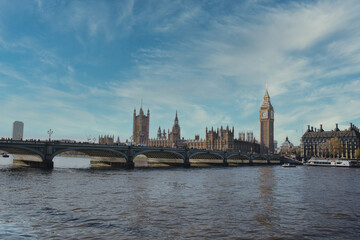 Westminster bridge crossing the river thames with big ben and the houses of parliament under a blue sky with some clouds in london, united kingdom