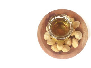 A clean jar filled Candlenuts essential oil with Dried Indonesian Candlenuts on wooden plate, or Kemiri in Indonesia, the seed of Aleurites moluccanus isolated on the white background. Copy space