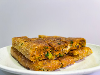 A platter of golden-brown martabak telur, a traditional Indonesian street food, is presented on a white plate. Each slice reveals a savory filling of egg, meat, chives, and other ingredients