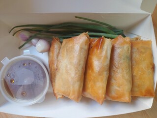 Lumpia or lunpia in paper box for take away, traditional snacks from Semarang, Central Java, Indonesia. Traditional spring rolls contain stir-fried bamboo shoots (rebung), eggs, and chicken or shrimp.