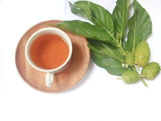 Noni fruit or Morinda citrifolia (Indian mulberry) with green leaves on tree branch on bamboo mat isolated on white background. Consuming boiled water of noni fruit juice can lower cholesterol levels