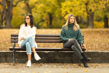 Two beautilful young women sitting on the bench in publiic park