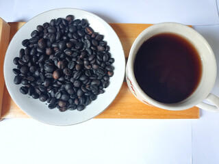 Roasted coffee beans and a cup of black coffee drink on a wooden plate on a wooden mat with white background