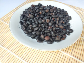 Roasted coffee beans on a white plate on bamboo mat with white background
