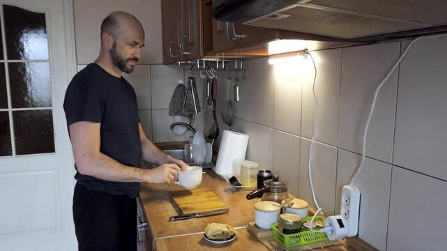A man in the kitchen takes a cup and pours tea