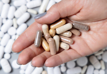Hand with brown and beige medical capsules over mix of white pills top view. Dietary supplements