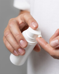 Woman squeezing hand cream on her finger and holding a cosmetic bottle in other hand, closeup