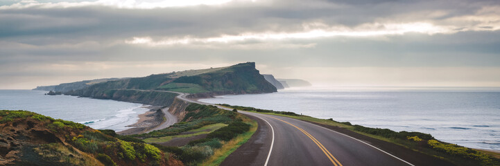 A winding road leads along a dramatic coastline with towering cliffs and a vast ocean.
