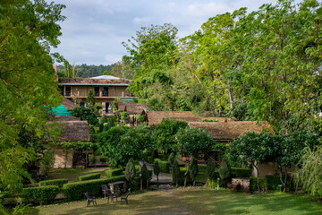 A serene resort nestled amidst lush greenery, rustic cottages with thatched roofs, manicured hedges and outdoor seating. The peaceful atmosphere for a nature retreat in Jim Corbett National Park India