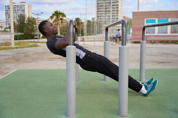 Young black man performing calisthenics on parallel bars in urban setting