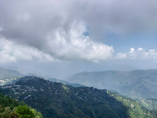 A scenic view of lush green mountains under a cloudy sky.Rolling hills dotted with houses create a serene and peaceful atmosphere, perfect for themes of nature, tranquility and outdoor beauty in india