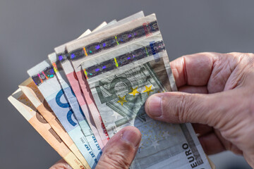 Stack of Euro banknotes of various denominations, being held by a person’s hands, on a plain grey background and copy-space.