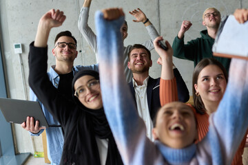A diverse team of business professionals ecstatically celebrating their success in a modern office, expressing triumph and unity after achieving their goals