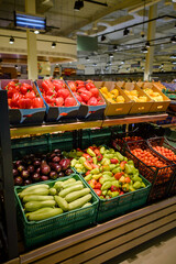 A vibrant display of fresh produce fills the shelves of a local grocery store. The colorful array of vegetables, including red and green bell peppers, eggplants, zucchini, and cherry tomatoes.