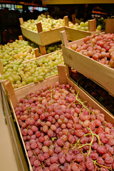 Crates overflowing with fresh green and red grapes are stacked in a supermarket, ready for sale. Focus on abundance and natural produce.