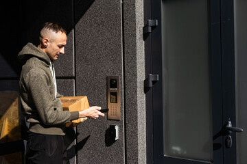 Man ringing intercom with camera near building entrance.