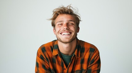 Obraz premium Smiling young man with tousled hair wearing an orange plaid shirt against a plain background