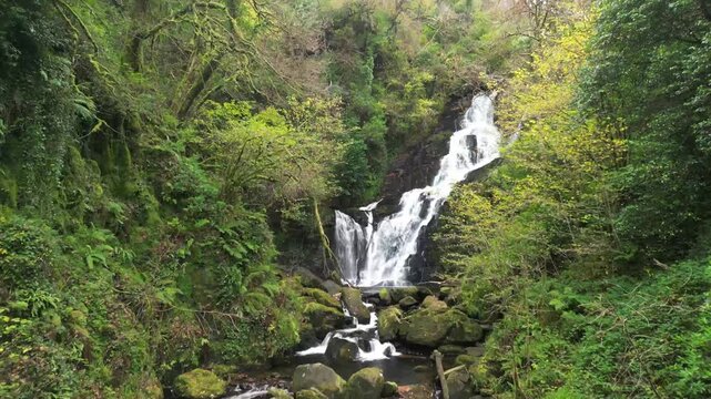 Stream of water from above cascading in a waterfall, Torc in Kerry county Ireland with a drone. Forest and rocks covered in moss