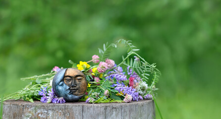 symbolic moon amulet and colorful wild flowers on stump, natural background. Wiccan magic practice...