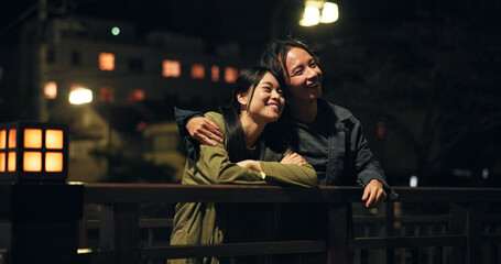 Bridge, couple and happy at night with hug for bonding, sightseeing and explore for fun in Japan. People, relationship and smile outdoor on evening date for fresh air, support and care as lovers © peopleimages.com