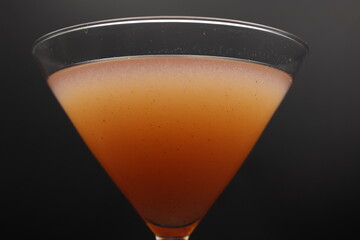 Close up on a pink craft cocktail in a martini glass with a. dark background. 
